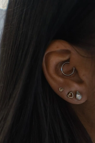 Daith piercing ezüst színű karikával, mellette három díszes fülcimpa ékszer (szív és csepp alakú köves), Soospierce munkája.